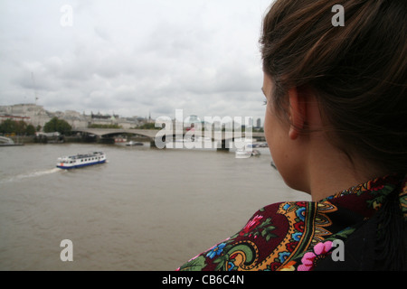 Sulla spalla il colpo da una donna che si affaccia alla Thames, London. Bridge, barca, sciarpa, bun, cielo grigio Foto Stock