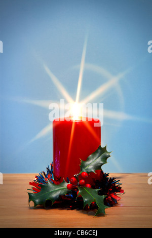 Foto di una candela di Natale e holly con raggiera, la stella dalla fiamma è stata creata nella fotocamera utilizzando un filtro. Foto Stock