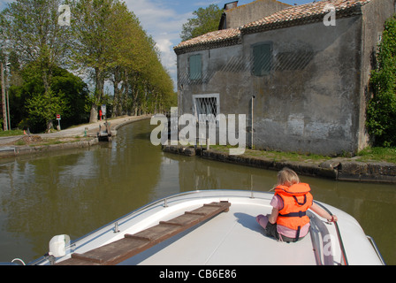 Fotografo della figlia di seduta sul ponte di prua di una casa galleggiante il viaggio sul Canal du Midi, passando una serratura vicino a Castelnaudary Foto Stock