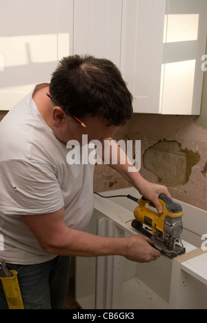 Tradesman utilizzando lo strumento seghetto alternativo per le unità di taglio per la cucina nuova installazione in casa residenziale, Bordon, Hampshire, Regno Unito. Foto Stock