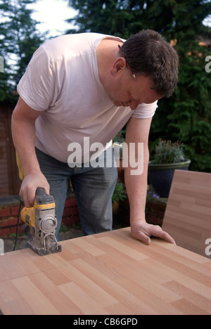 Tradesman usando una sega per tagliare il piano di lavoro per il montaggio in cucina nuova installazione in casa residenziale, Bordon, Hampshire, Regno Unito. Foto Stock