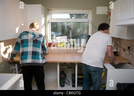 Tradesman (a destra) e il suo assistente il posizionamento del piano di lavoro in cucina nuova installazione in casa residenziale, Bordon, Hampshire, Regno Unito. Foto Stock