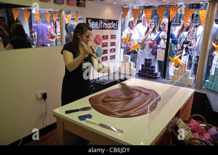 Con una folla di spettatori, una giovane donna fa un lotto di fudge con la mano in Roly's Fudge negozio Il Watergate Street, Chester, Regno Unito. Foto Stock