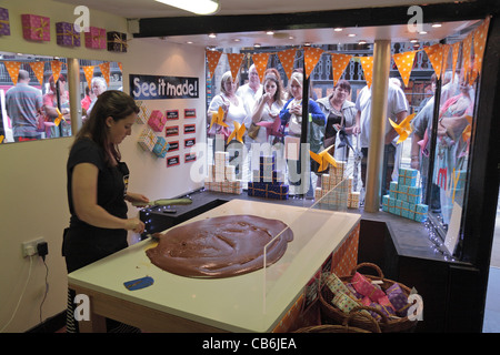 Con una folla di spettatori, una giovane donna fa un lotto di fudge con la mano in Roly's Fudge negozio Il Watergate Street, Chester, Regno Unito. Foto Stock