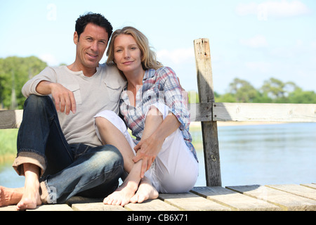 Età media giovane seduto su un pontone vicino a un lago Foto Stock