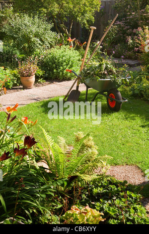 Lavorare nel giardino estivo al mattino con la carriola, pala e rastrello - verticale Foto Stock