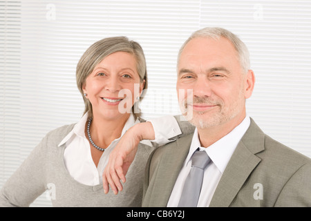 Professional elegante sorridente senior imprenditrice appoggiata contro il suo collega di sesso maschile Foto Stock