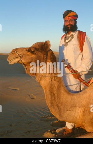 Signor deserto in tradizionale Rajput, Rajasthani, in piedi accanto a un cammello sulle dune di sabbia vicino a Jaisalmer, Rajasthan, India Foto Stock