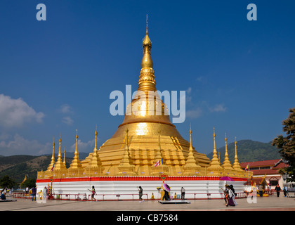 Oro gigante stupa di Tachileik Shwe Dagon Pagoda in Myanmar luccicante nella luce del sole con le persone camminare e pregare nei santuari Foto Stock