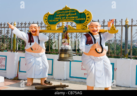 Statue di 2 fat sorridente uomini in abiti bianchi tenendo un polo di oro fino con una campana a Tachiliek Shwe Dagon Pagoda in Myanmar Foto Stock