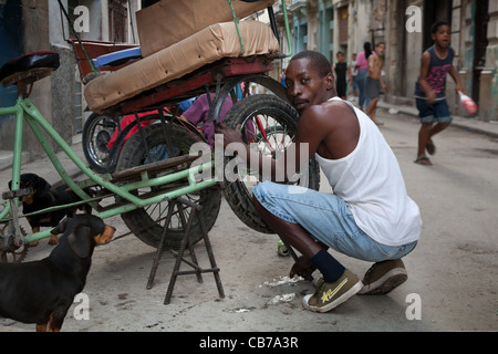 Un uomo che fissa il pneumatico di una 'Bicitaxi','Avana (La Habana, Cuba Foto Stock