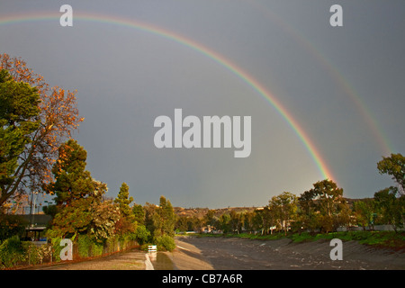 Un doppio arcobaleno su tempesta lo svuotamento di acqua dai tubi di tempesta in Ballona Creek, Culver City, CA Foto Stock