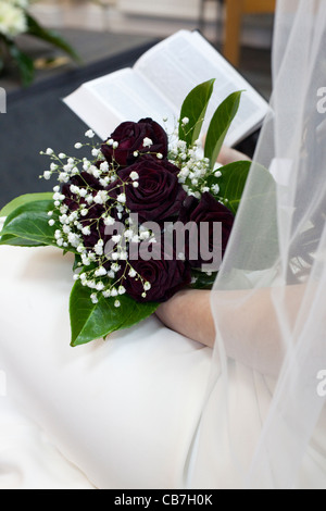 Una sposa tiene nelle sue mani wedding bouquet di rose rosse e leggere la Bibbia. Foto Stock