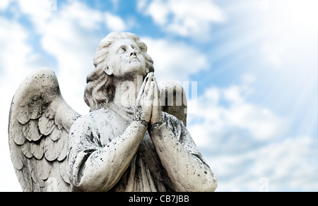 Bella statua dell'Angelo in preghiera, il cielo blu con nuvole e sole con raggi in background Foto Stock