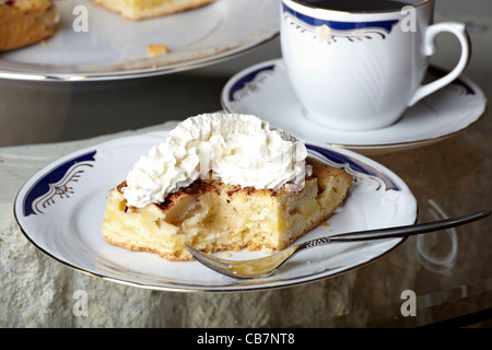 Torta di mele con panna montata su una piastra e un set da caffè sul tavolo Foto Stock