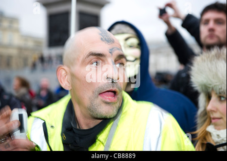 Testa calva tatuato uomo con piercing indossando giacca riflettente avente divertimento presso il settore pubblico di marzo a Londra. Foto Stock