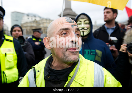 Testa calva tatuato uomo con piercing indossando giacca riflettente avente divertimento presso il settore pubblico di marzo a Londra. Foto Stock