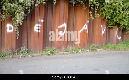 Le parole déjà vu spruzzato in bianco come graffiti su un arrugginito, inaccessibili costruttivo di muro di ferro con una verde pianta rampicante Foto Stock