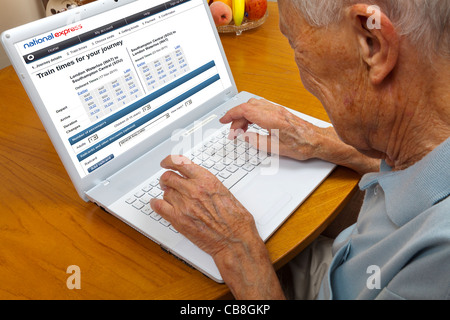 Anziano gentiluomo navigare sul web di prenotazione viaggi in pullman su un computer portatile Foto Stock