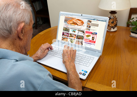 Anziano gentiluomo navigare il web alla ricerca di idee di cottura su un computer portatile Foto Stock