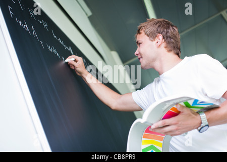 Bello studente di college per risolvere un problema di matematica durante le lezioni di matematica di fronte la blackboard/lavagna (toni di colore immagine) Foto Stock