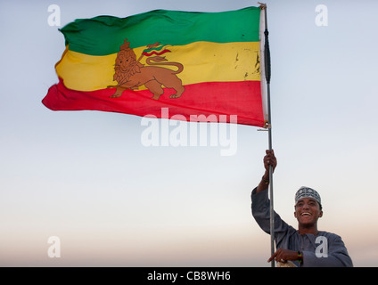 Ragazzo adolescente brandendo bandiera etiope, Rastafari Lion, mentre sorride alla fotocamera, Lamu, Kenya Foto Stock