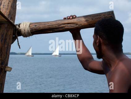 Retro di un uomo guarda orizzonte, due Dhow a vela in rassegna, Lamu, Kenya Foto Stock