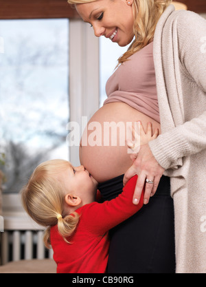 Piccola figlia bacia felice in stato di gravidanza della madre ventre Foto Stock