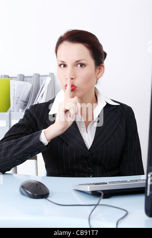 Vista frontale di un bel business donna seduta dietro la scrivania, mostrando di essere silenzioso. Foto Stock
