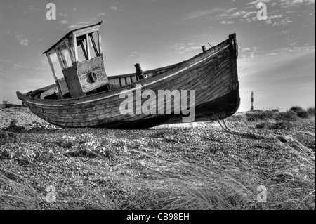 Un vecchio abbandonato la pesca in barca sulla spiaggia di Dungeness, Kent, Regno Unito. La Dungeness faro è in background. Foto Stock