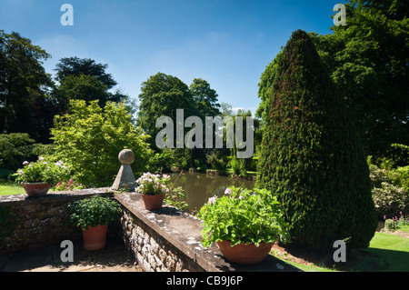 Una terrazza fortificata piantati con vasi di terracotta che si affaccia sul laghetto ornamentale a Coton Manor Gardens, Northamptonshire, Inghilterra Foto Stock