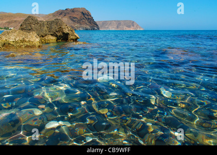 Una bella vista dalla Playa de Las Negras Spiaggia, mostrando le cristalline acque del Mediterraneo, scogliere di rocce e pietre di colore nero Foto Stock