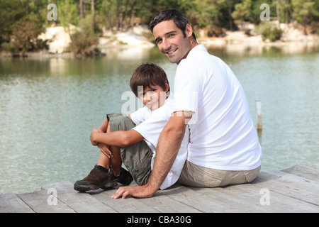 Un padre e suo figlio seduto su un pontone si trova di fronte ad un lago Foto Stock