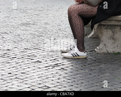 Giovane donna con il pattern calze collant seduta sul banco in strada in città città Foto Stock