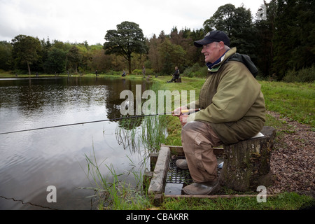 Anziano pescatore pesca in una piccola pesca loch, Kilmarnock, Ayrshire, in Scozia Foto Stock