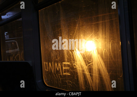 Vista dall'interno carrello tubo guardando verso una luce che illumina i graffiti sulla finestra del treno. Il vandalismo 'attacco su di me' Foto Stock