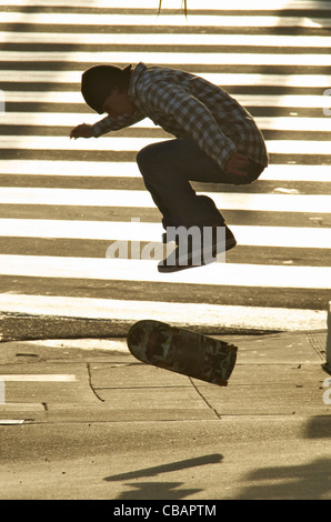 Un maschio di guidatore di skateboard facendo un Ollie jump trick su un marciapiede. Foto Stock