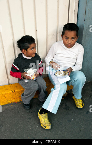 Due luminose eyed giovane messicano vecchi e giovani fratelli seduti sul marciapiede stoop mangiare pranzo quartiere Roma Città Del Messico Foto Stock