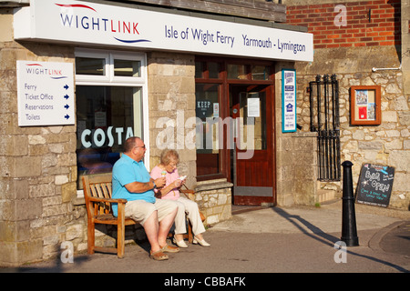 Coppia matura seduto su panchina godendo di gelati al di fuori del terminal dei traghetti Wightlink a Yarmouth, Isle of Wight, Hampshire UK nel mese di settembre Foto Stock