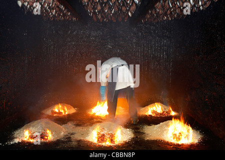 Un uomo pile di luci di trucioli e segatura di legno di quercia in un forno di fumare presso l Robsons e figli a Craster, Northumberland. Foto Stock