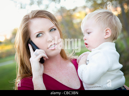 Sottolineato donna attraente utilizzando il telefono cellulare con il bambino nelle braccia. Foto Stock