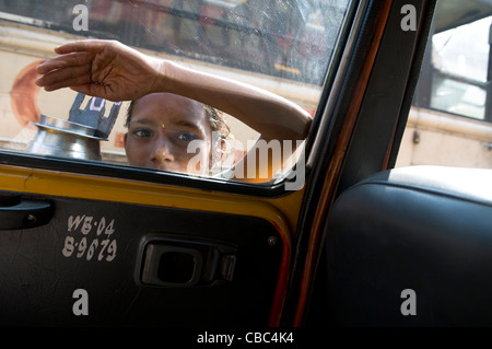 Un giovane mendicante a bussare alla finestra e taxi su una strada trafficata in Kolkata. Foto Stock