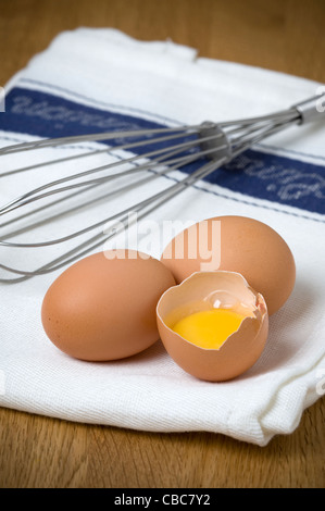 Brown uova di galline su un tè bianco asciugamano con un acciaio inossidabile Sbattere un uovo rotto e separata che mostra il bianco d'uovo e il tuorlo d'uovo Foto Stock