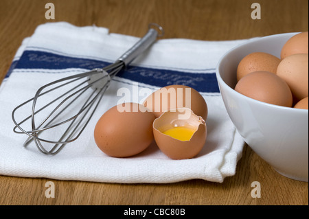 Brown uova di galline su un tè bianco asciugamano con un acciaio inossidabile Sbattere un uovo rotto e separata che mostra il bianco d'uovo e il tuorlo d'uovo Foto Stock