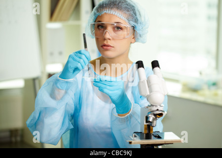 Fiducioso medico di studiare nuove sostanza in laboratorio con apparecchiature da laboratorio in mani e vicino al microscopio da Foto Stock