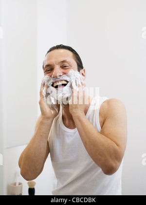 Uomo sorridente di schiumeggiamento della sua barba Foto Stock