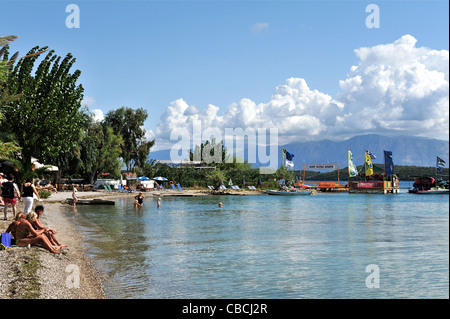 Le persone che si godono la stretta striscia di spiaggia di ciottoli a Nidri sull'isola del Mar Ionio di Lefkas, Grecia. Foto Stock