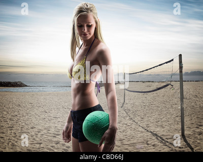Donna che trasportano pallavolo sulla spiaggia Foto Stock