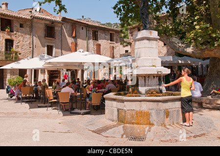 Le persone che si godono le bevande su un caldo summerday presso un cafe' sul marciapiede da fontana in cima della collina villaggio di St Guilhem le Desert Foto Stock