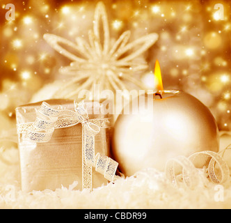 Golden decorazione di Natale, caldo incandescente sfondo vacanze con candela e confezione regalo su sognanti luci bokeh di fondo Foto Stock